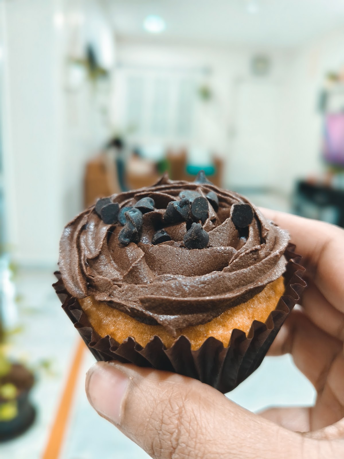 A chocolate-chip cupcake with swirled chocolate frosting, held up in the bakery kitchen
