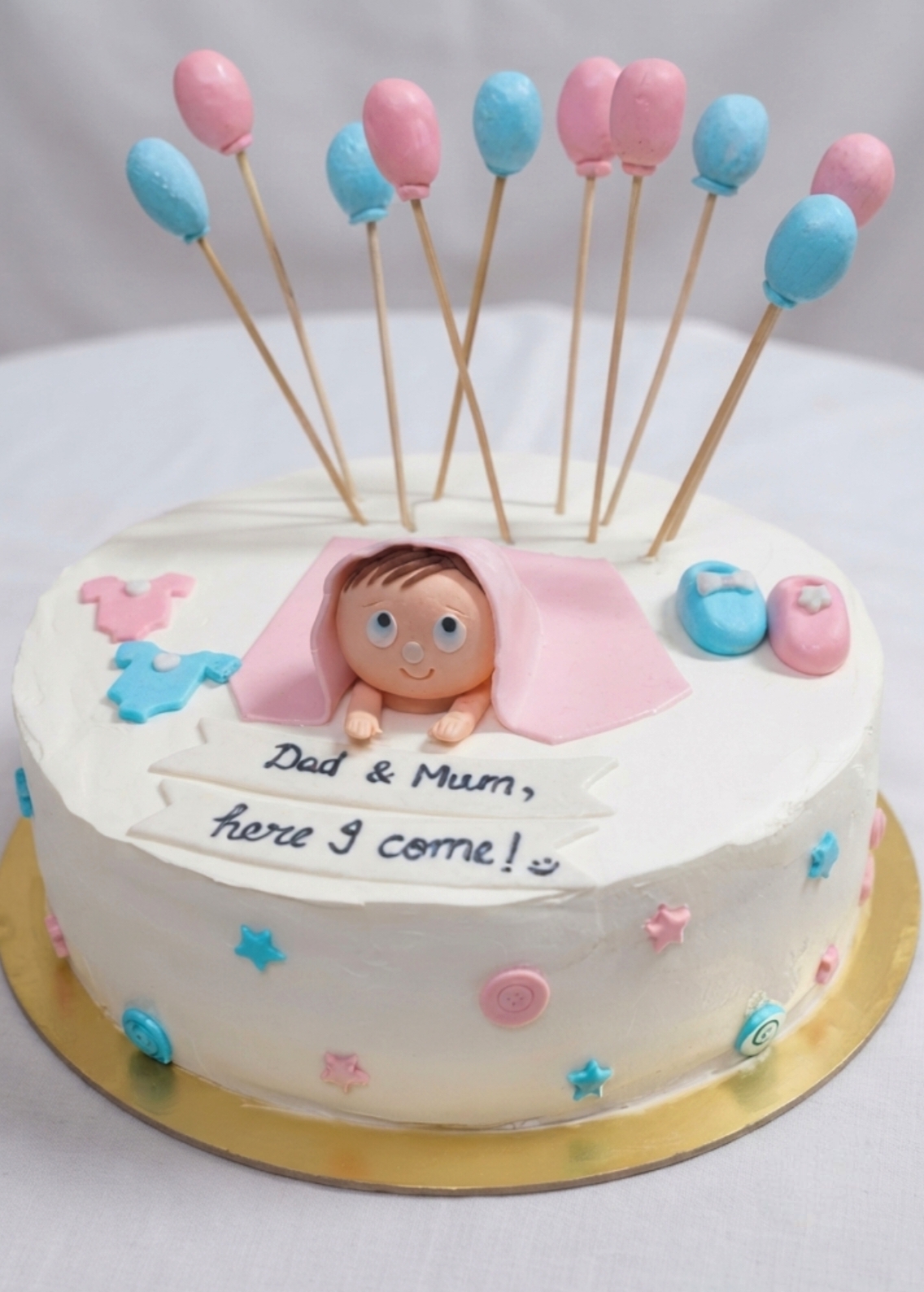 White baby-shower cake with pink and blue balloon toppers and a fondant baby