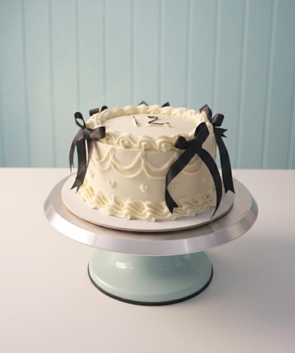 White vintage-style cake with piped buttercream borders and black ribbon bows