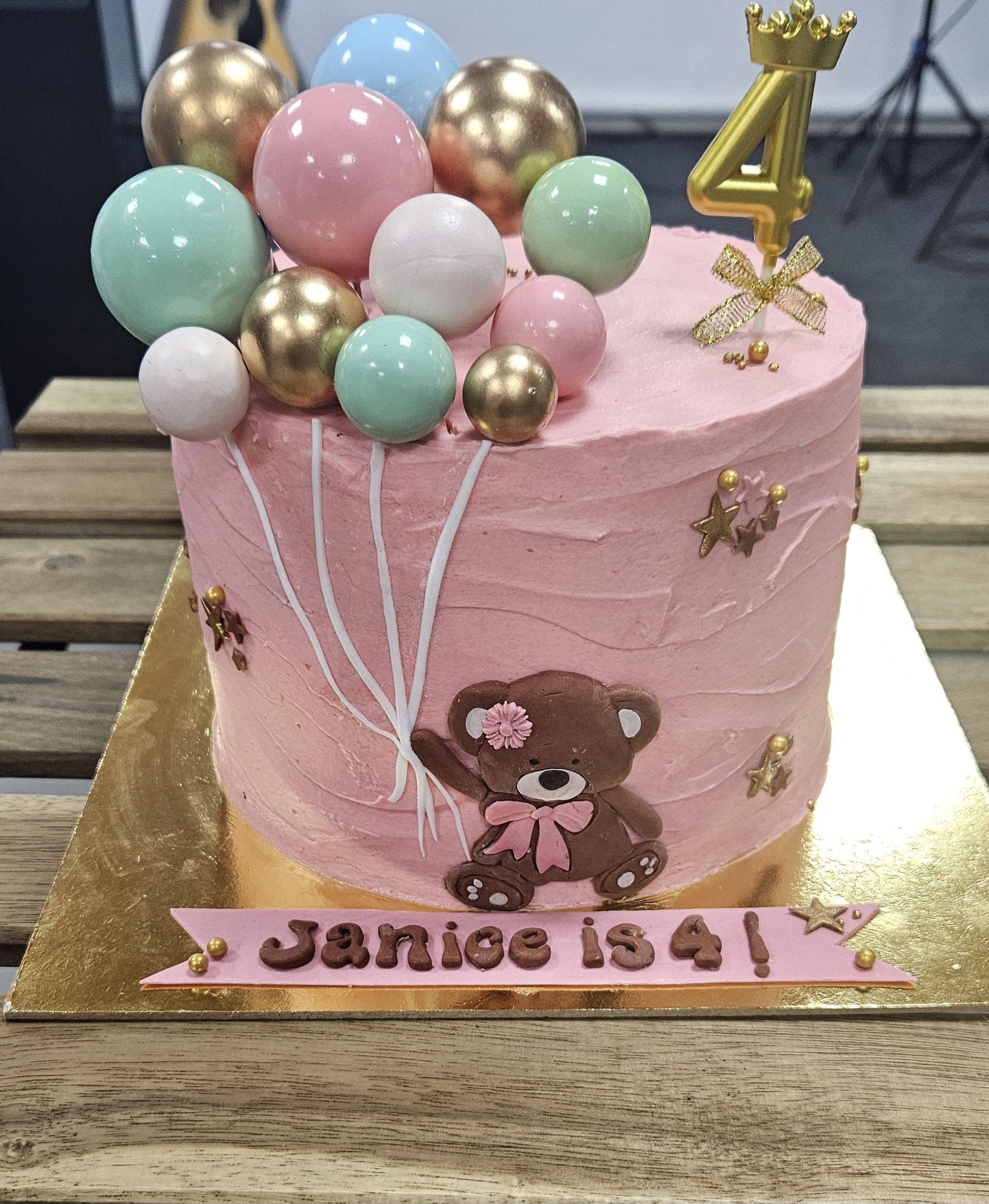 Pink teddy-bear birthday cake with balloon toppers and a gold number-four candle