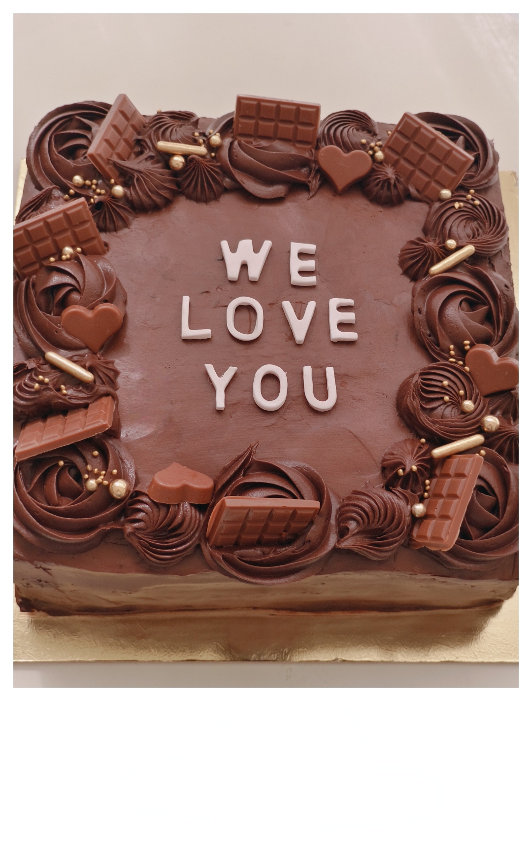 Square chocolate cake decorated with piped rosettes, chocolate bars, and hearts